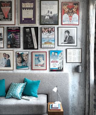 Wall with many framed theatre prints and photographs above a grey sofa with green cushions