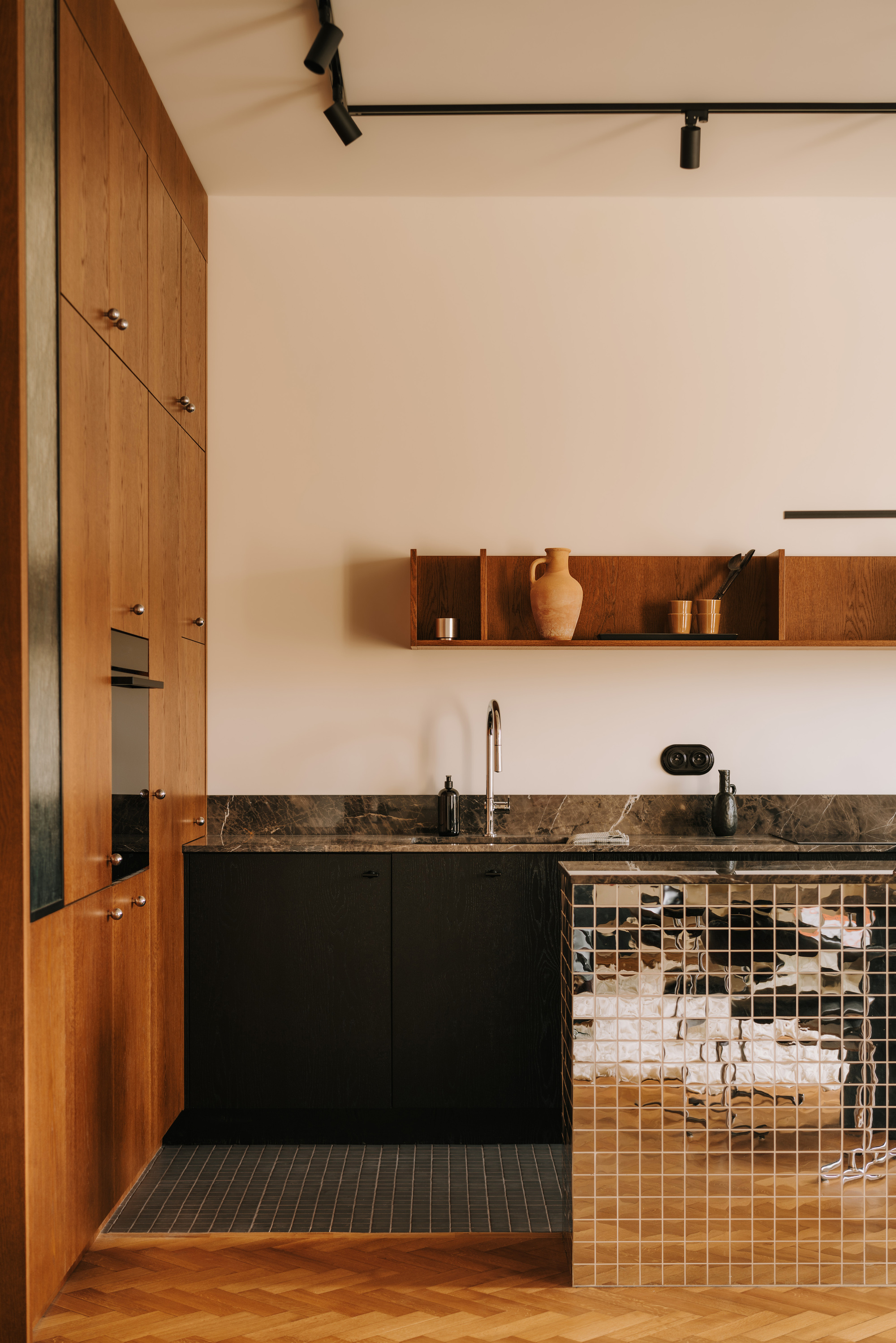 Image of a wooden kitchen with black cabinetry and a kitchen island that is covered in mirrored subway tiles.