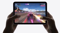 Hands holding an iPad mini 6, playing a racing game