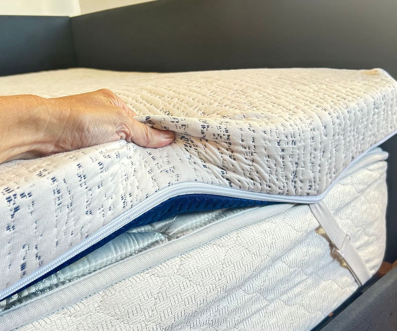A hand seen squeezing the blue and white Viscosoft High-Density Mattress Topper on a white mattress with white corner straps.