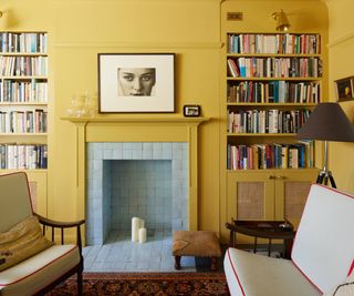 living room with yellow walls, alcove shelving and pale green tiled empty fireplace with yellow mantle