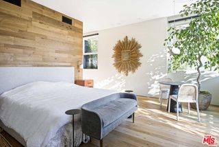 A bedroom with a wooden room divider behind the headboard, white walls, and a sun-shaped mirror on the wall