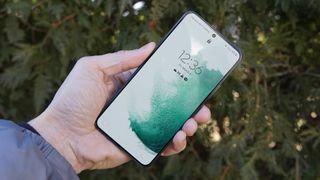 Samsung Galaxy S22 ihmisen kädessä vihreää kasvustoa vasten