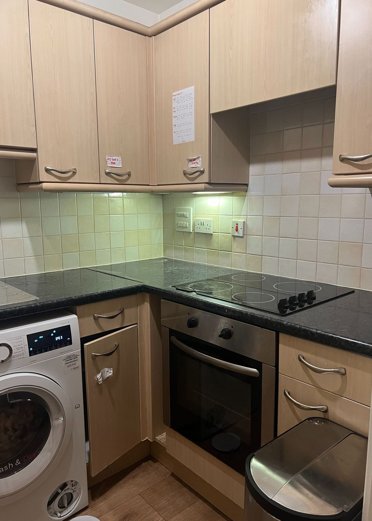 A kitchen with wooden/oak features. In the image you can also see the washing machine, stove, bin and oven