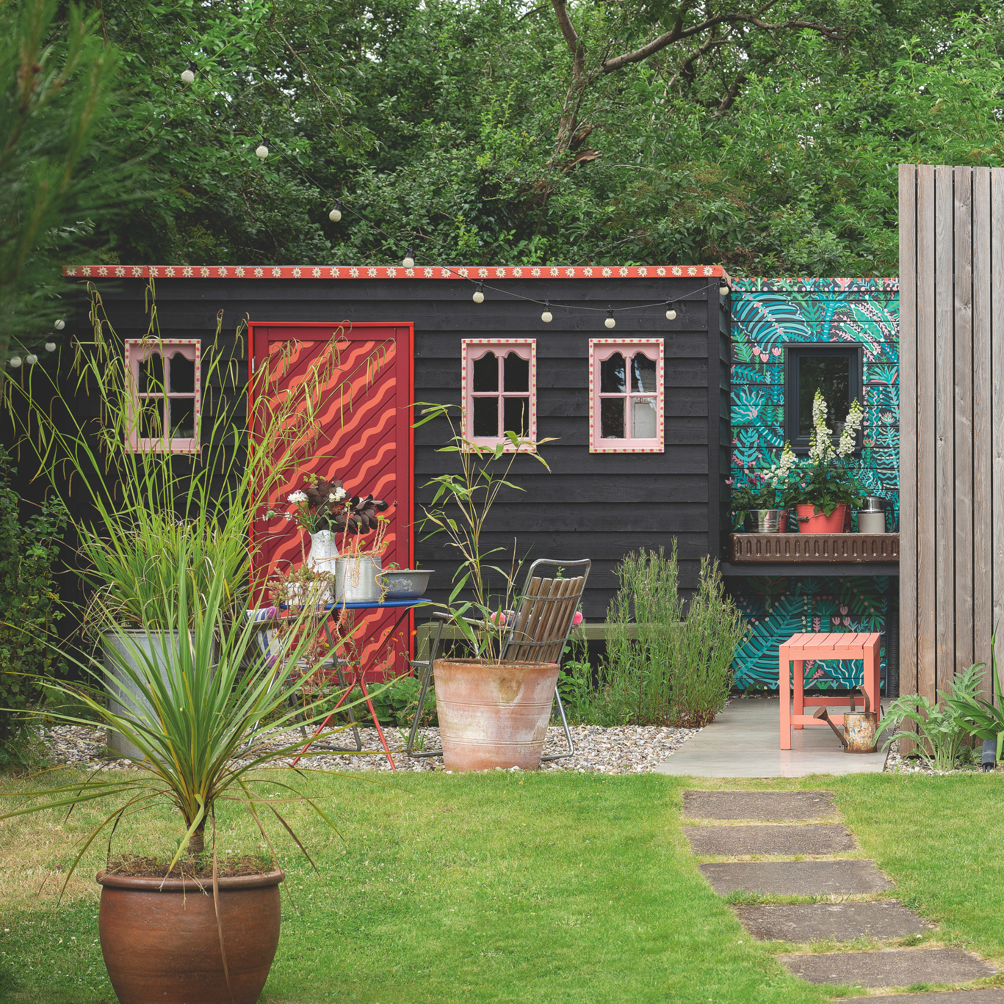 Black garden shed with a red striped door and roof.