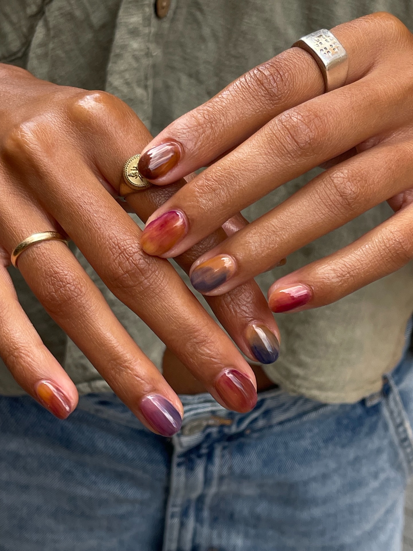 Short rounded nails with blurry patches of rust, blue and gold polish, rings on the fingers
