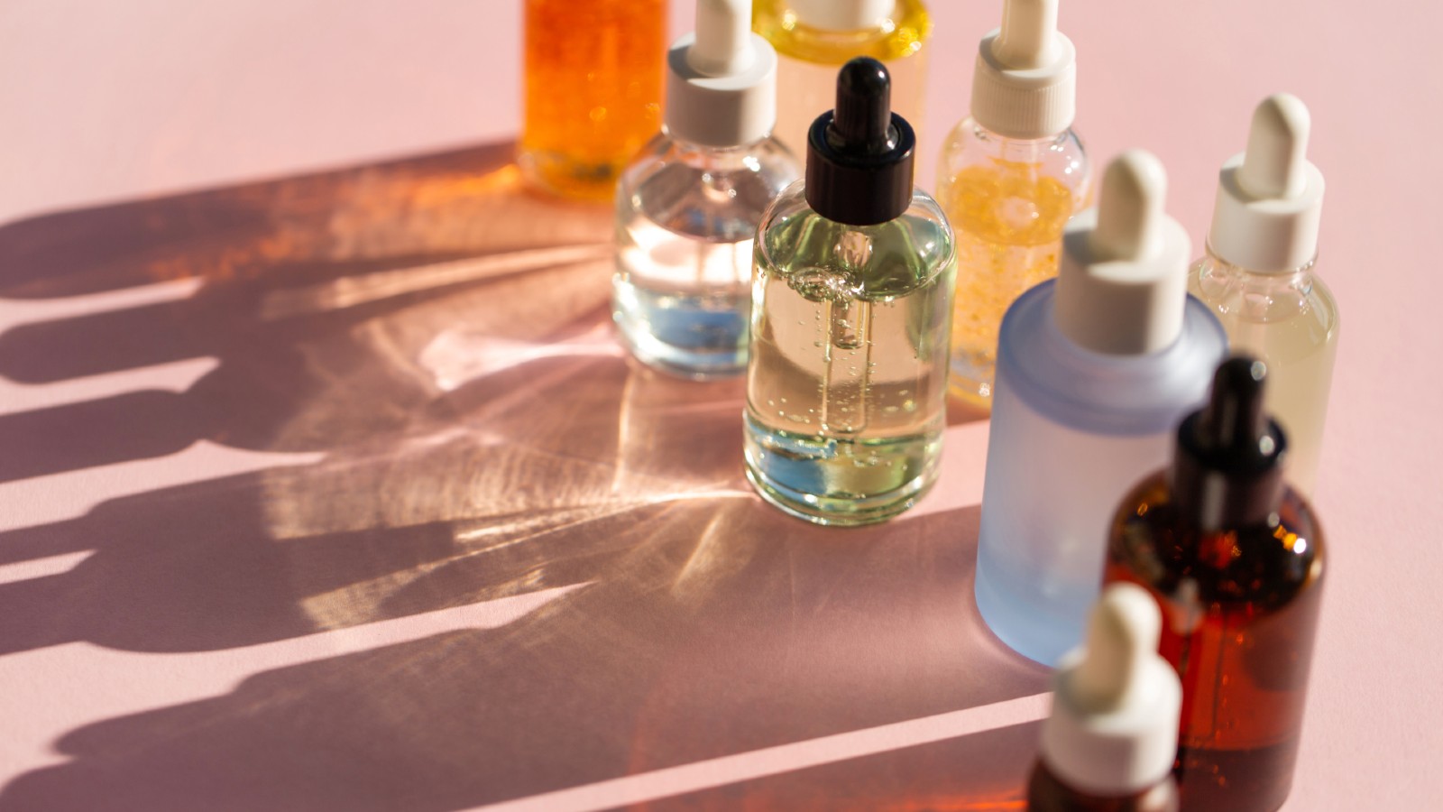 Bottles of cosmetic products on pink background. Trendy selfcare products of the year