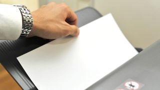 Man's hand with watch visible holding a piece of paper in a compact printer.