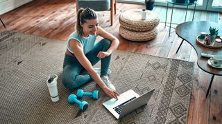 a photo of a woman looking at her laptop before doing a home workout
