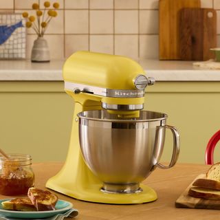 Yellow KitchenAid on wooden table with green kitchen