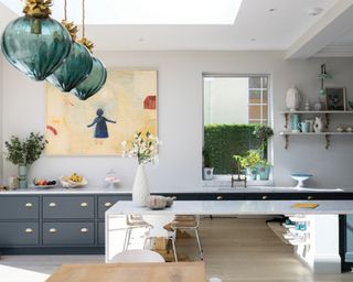 A blue-grey kitchen with trio of teal ceiling pendant lights and wall art