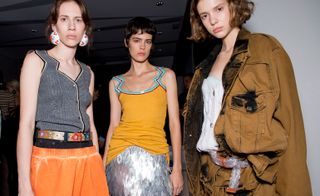 Models wear grey top with orange skirt, orange top and sequinned silver skirt, brown jacket and trousers with white top