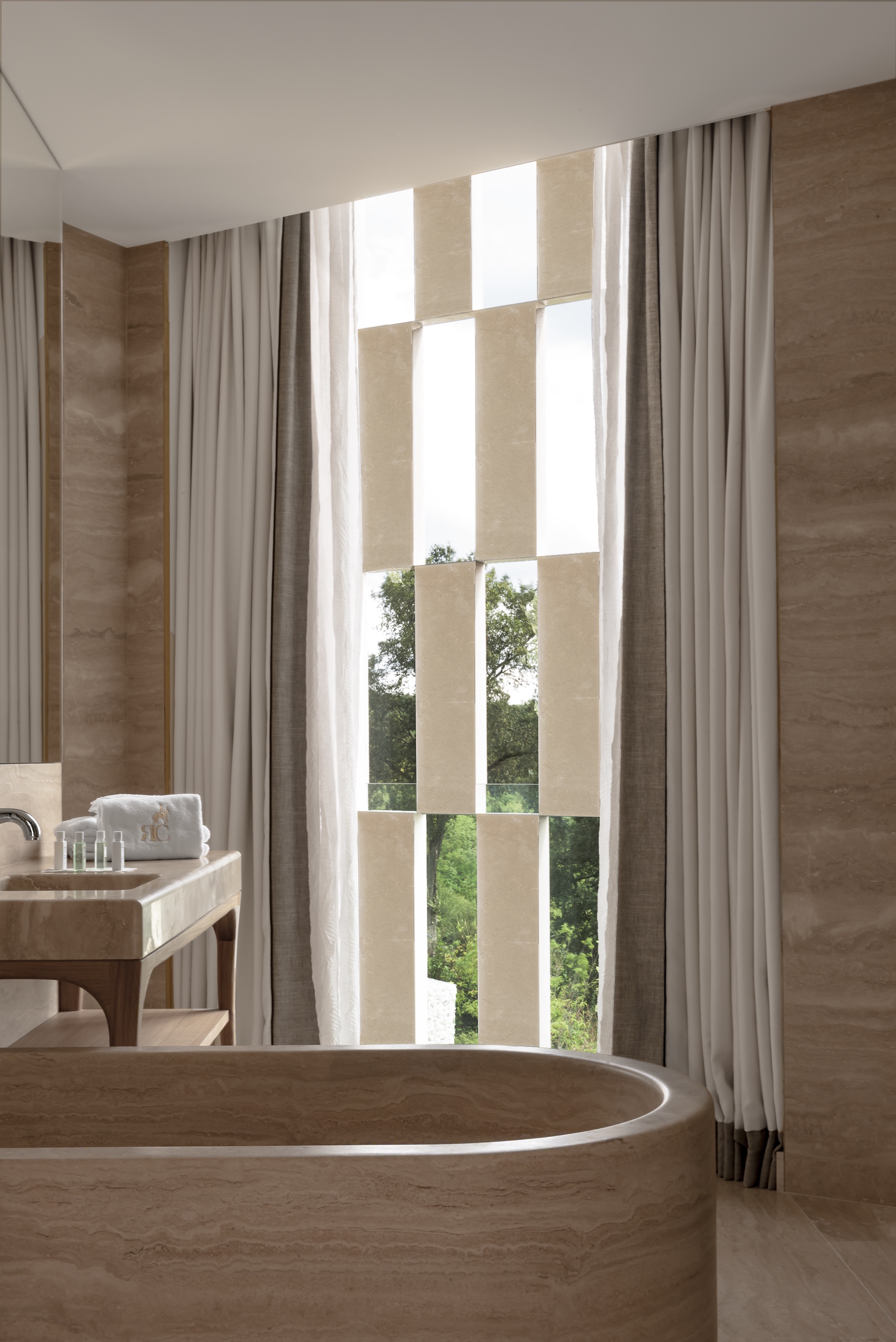 A minimalist hotel with cream tones throughout boasts floor-to-ceiling windows, historical accents, and a naturally lit atmosphere.