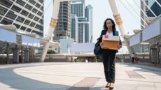 Female worker leaving office while carrying belongings in a cardboard box after being made redundant.