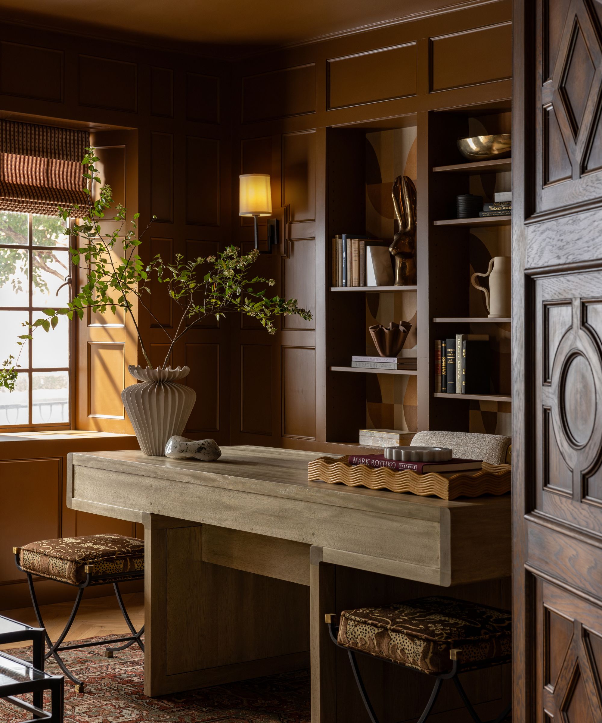 A moody home office with dark ochre walls and a wooden desk.