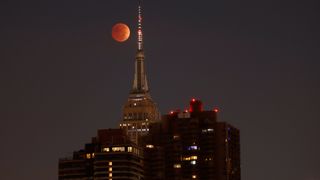 red moon behind tall buildings during total lunar eclipse. 