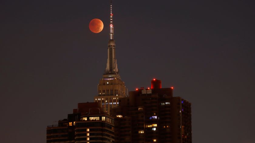  red moon behind tall buildings during total lunar eclipse. 