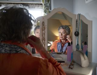 Anne (Barbara Flynn) sits at her dressing table, looking into her mirror as she puts on her earrings