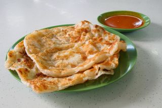 A plate with two roti canai flatbreads on it with a small bowl of curry next to it