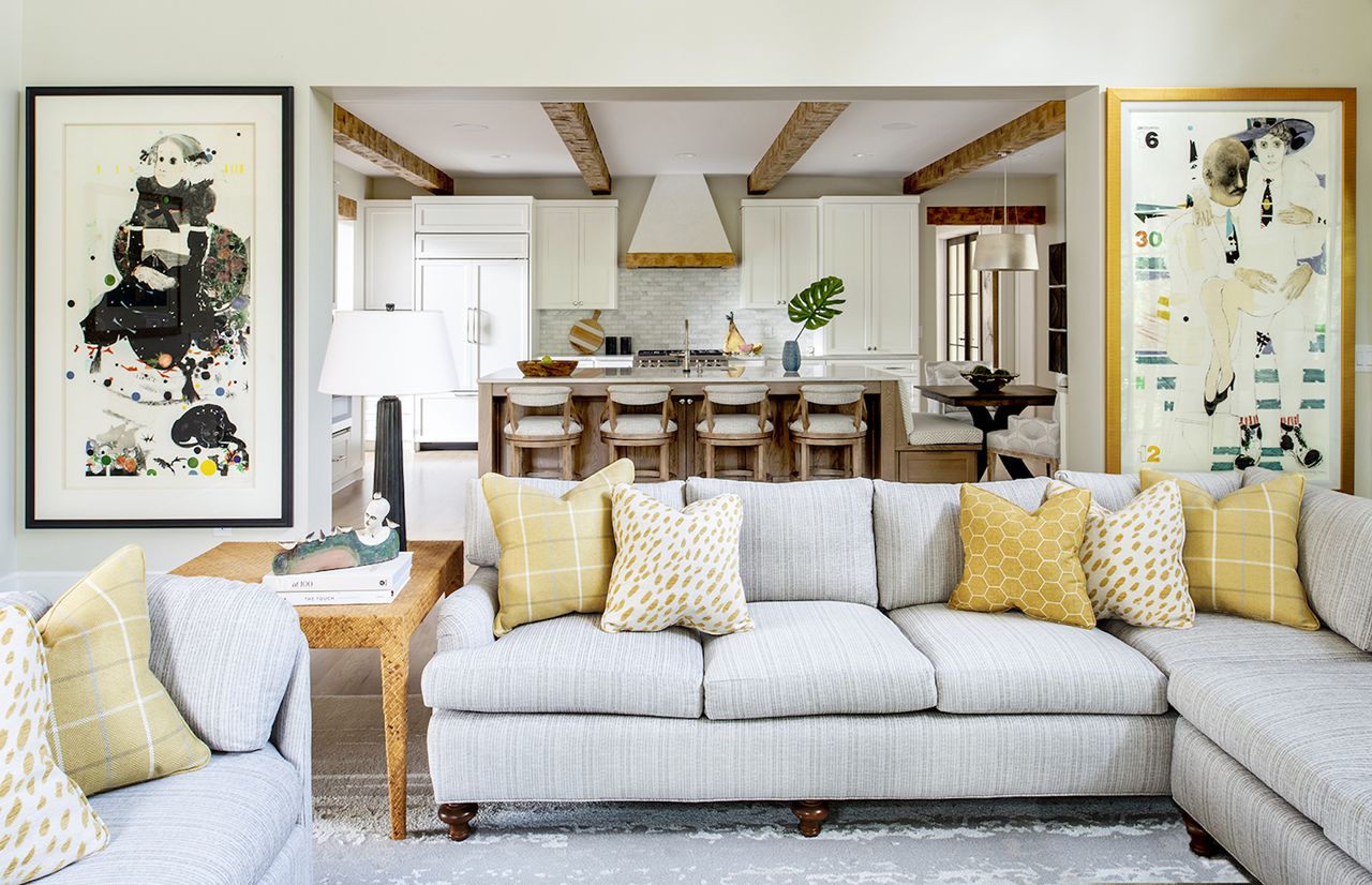 living room with grey sectional sofas, artwork, kitchen in the background