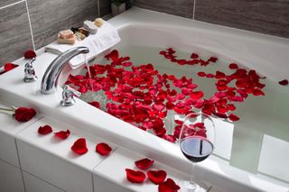 A bathtub filled with water and rose petals.