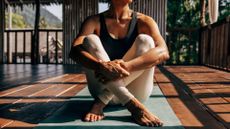 Woman sitting on yoga mat with hands clasped over legs, about to set up for the side plank exercise, looking out into studio
