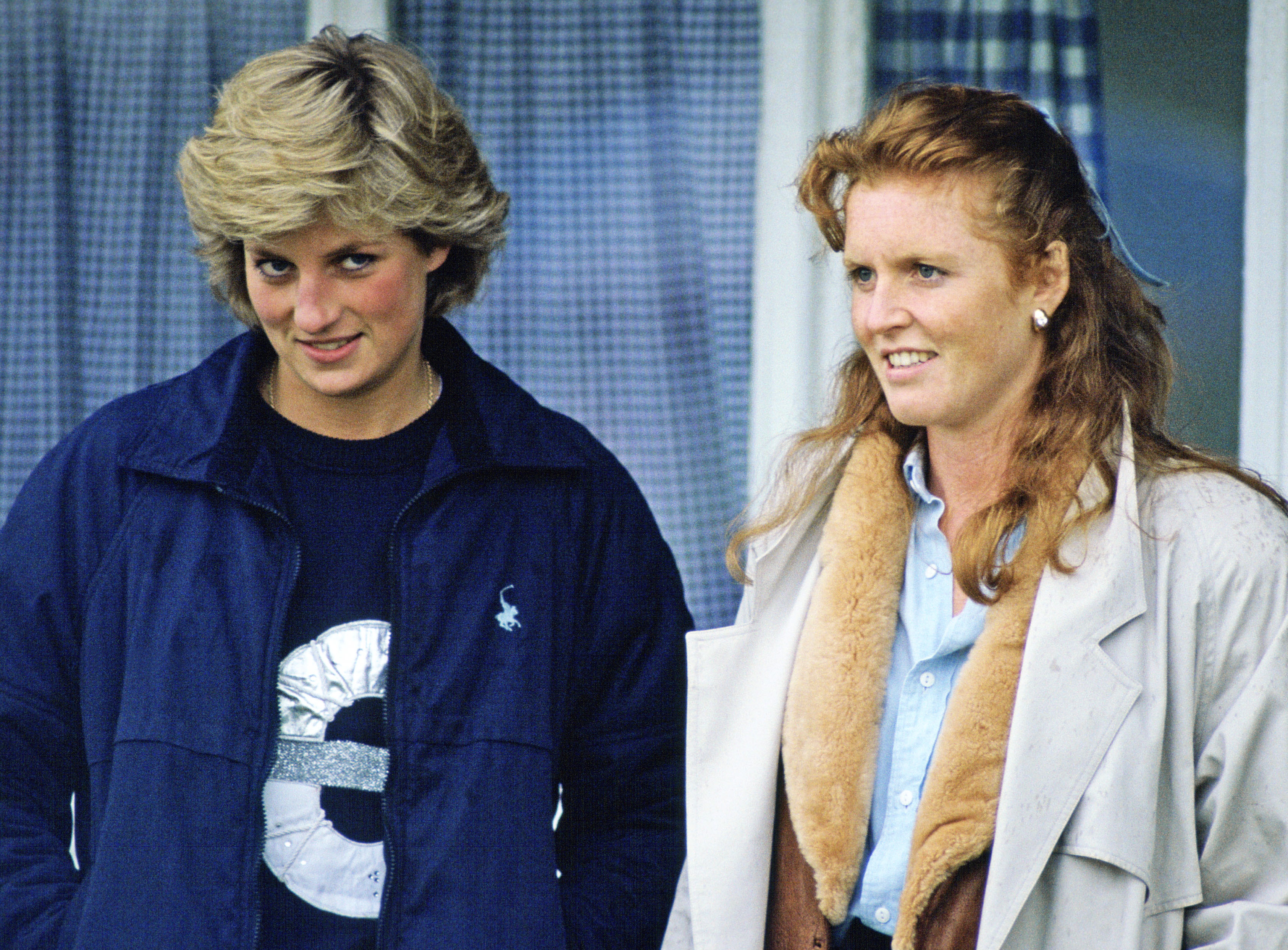 Princess Diana standing wearing a blue jacket standing next to Sarah Ferguson in 1987