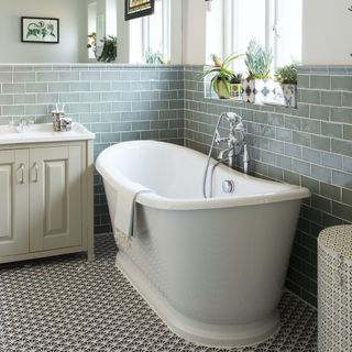 Green tiled bathroom with white freestanding roll top bath and plants on windowsill