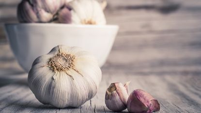 A white garlic bulb alongside two purple garlic cloves