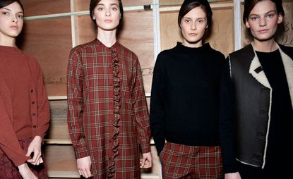 Four models - one in a red jumper and skirt, one in a red chequered dress, one in a black jumper and red chequered trousers, and one in a black top with a black gilet with fleece lining