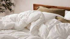 A comforter on a bed with brown and white pillows against a white wall.