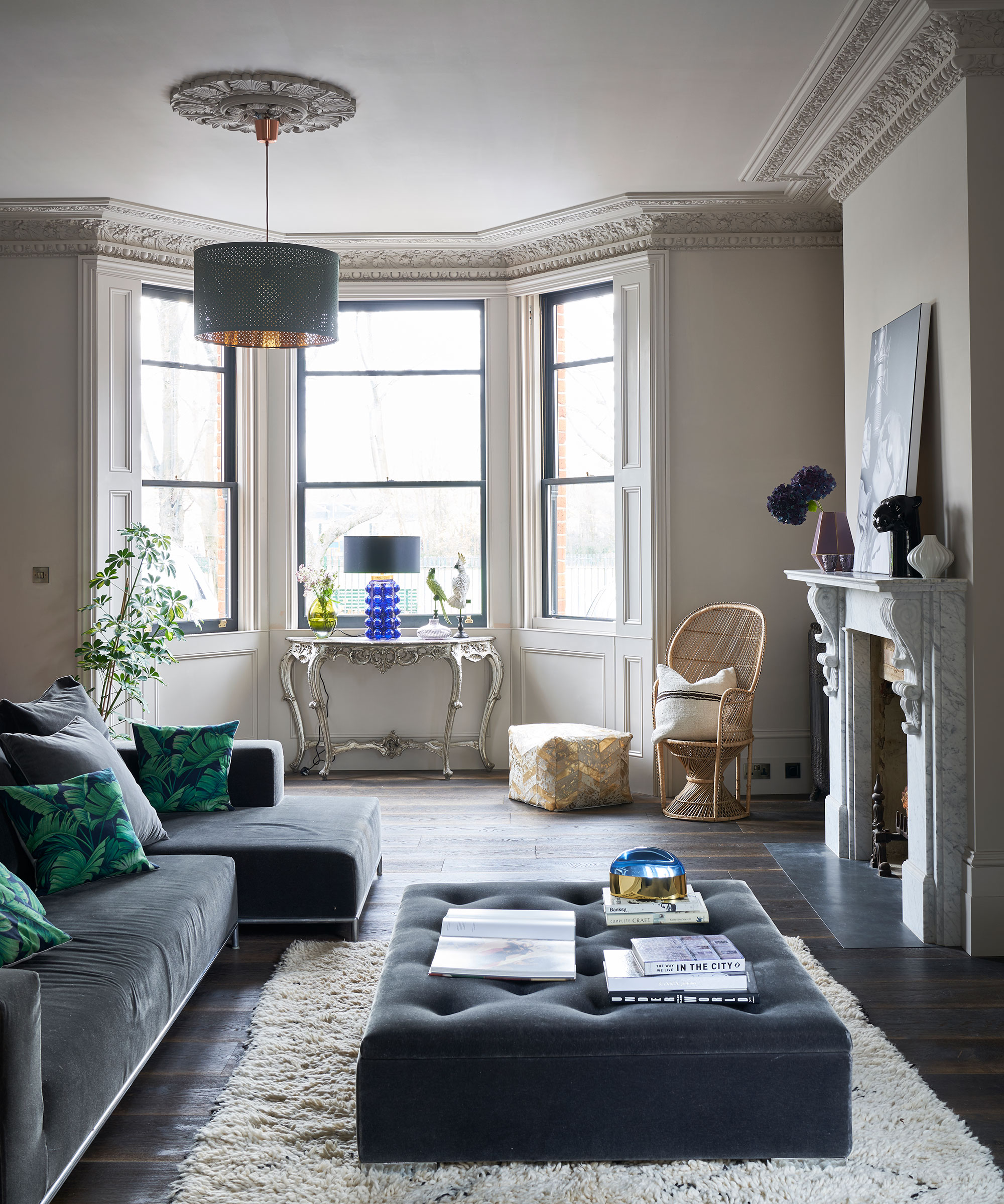 A beige living room with colorful dark blue and teal furnishings and architectural details including cornicing and a marble fire place.