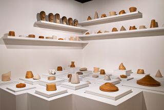 View of the Musée Yves Saint Laurent Paris tribute featuring several small wooden objects on plinths and shelving in a room with light coloured walls