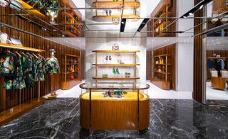 Interior view of the Dolce & Gabbana Canton Road boutique in Hong Kong. The space features black marble and white flooring, wooden display units with fashion accessories, rails with clothing and a mirrored ceiling