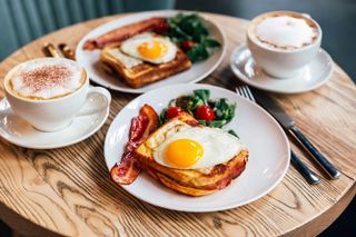 A round wooden table with toast, bacon, fried eggs, and coffees.