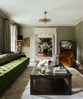 A moody living room with a green couch, a chandelier and artwork in gold frames