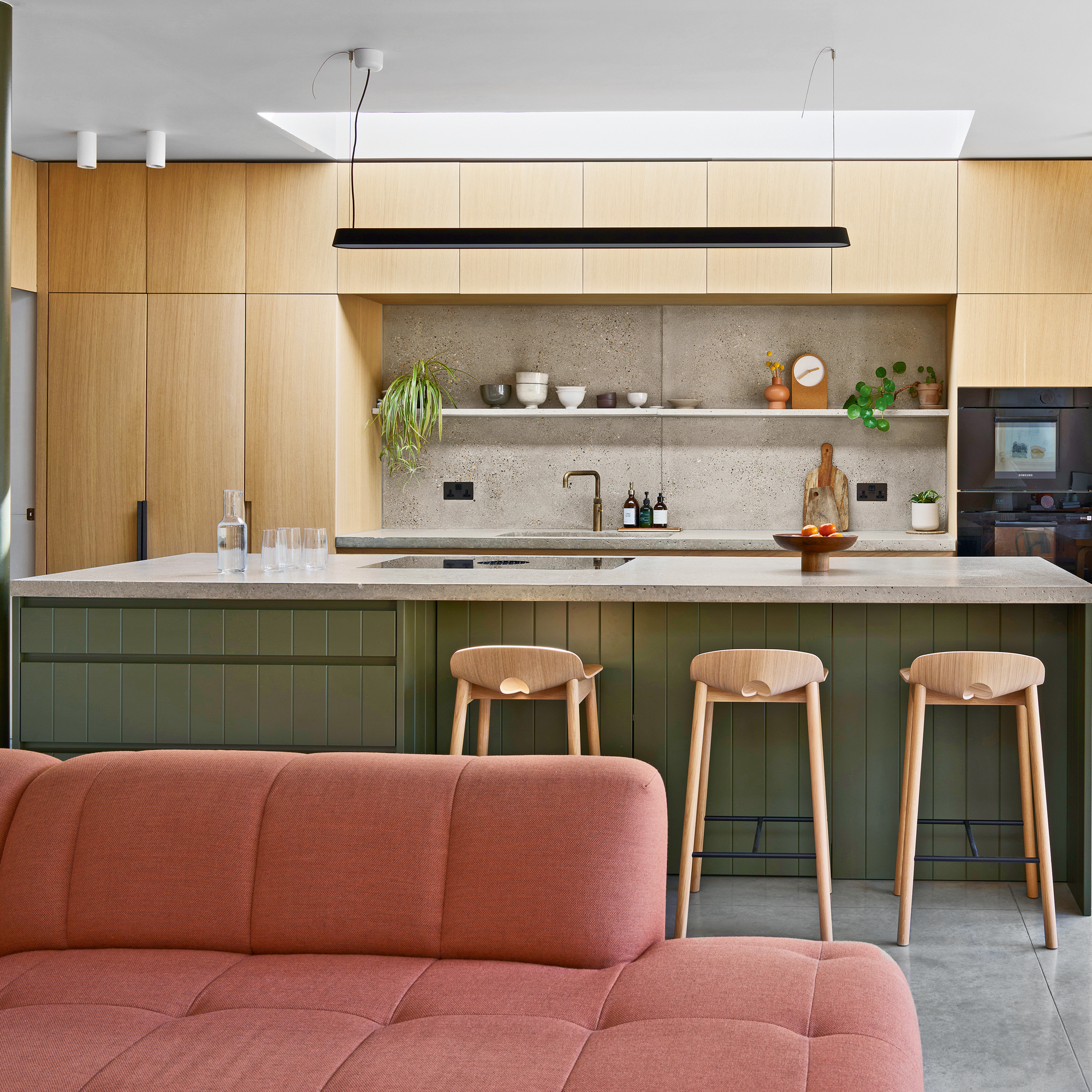 an open plan kitchen and living area with a dusky pink sofa and a large kitchen island with three bar stools