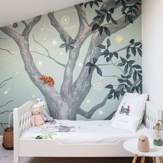 White cot in front of painted mural wall with tree design