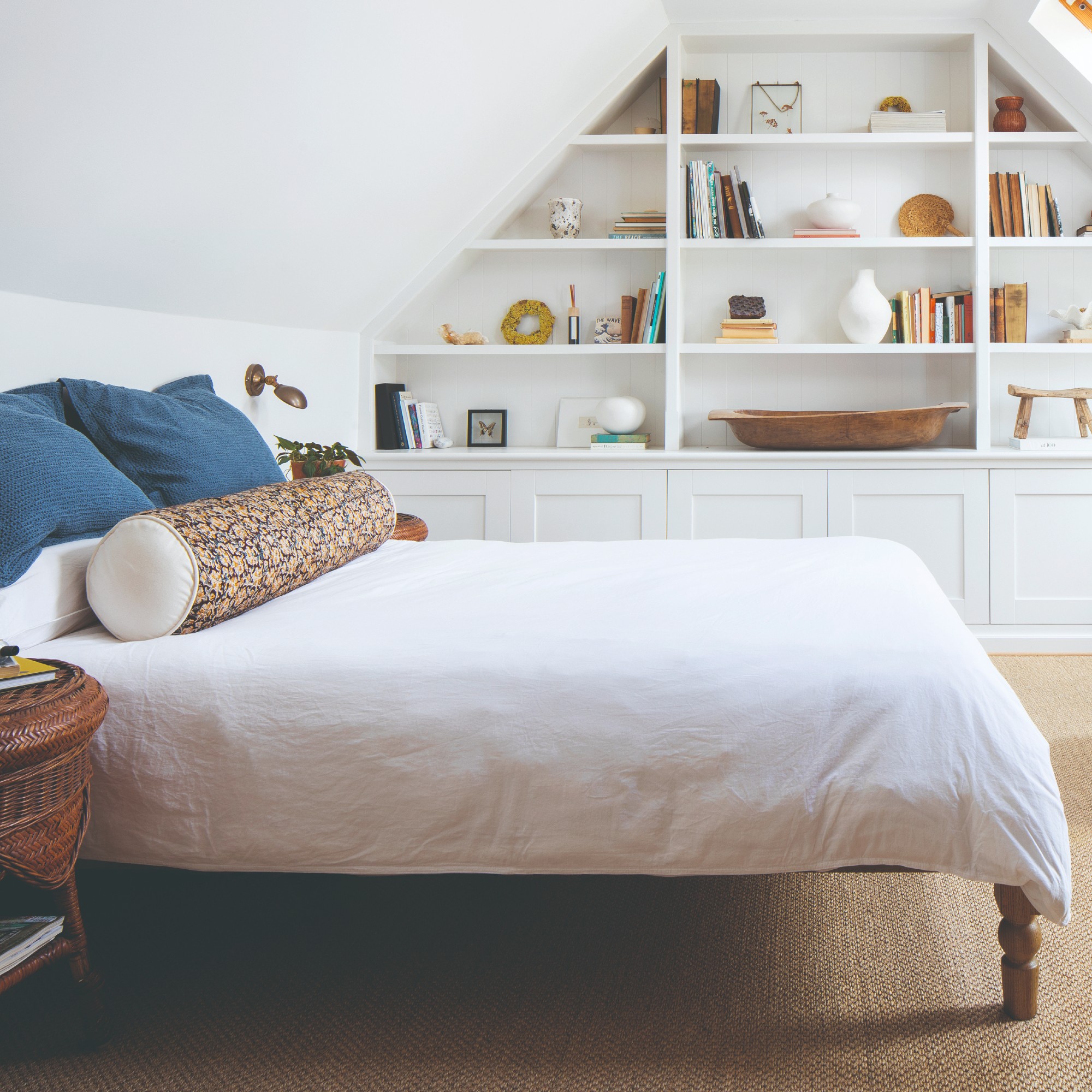 A white attic bedroom with a bespoke built-in bookcase displaying books and decorative objects
