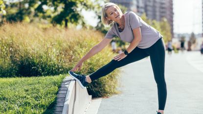 Woman stretches her hamstring on low wall outside