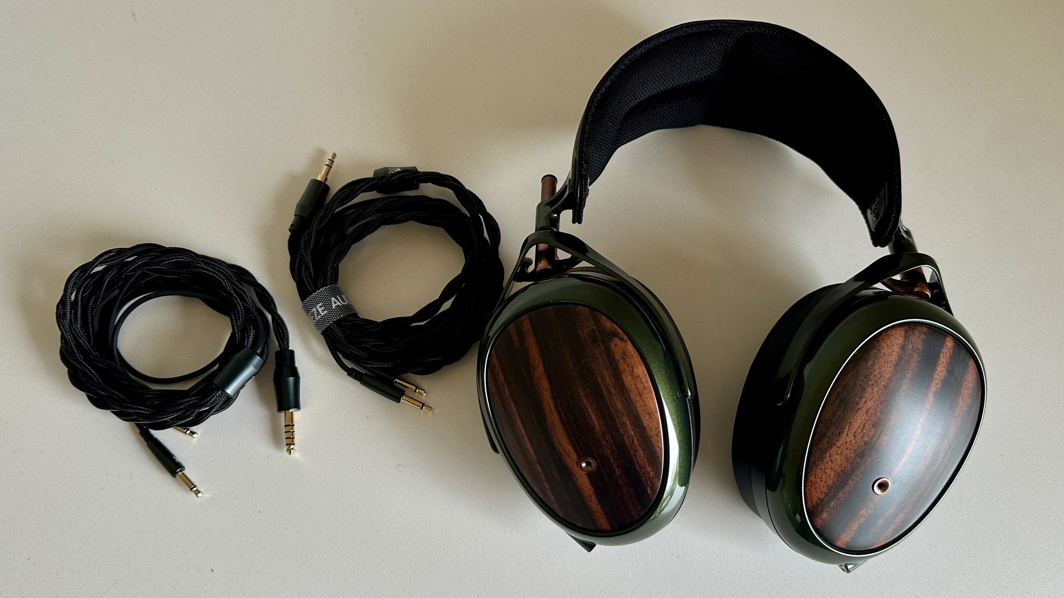 Meze Audio Strada headphones with wooden ear cups, in close-up and with their case and cables visible, on a white table