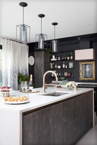 A metallic grey and black kitchen scheme with three boxy pendant ceiling lights over kitchen island with built-in sink