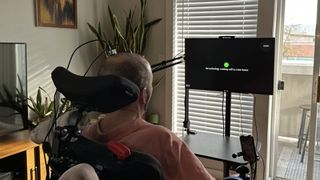 A man in a wheelchair with wires around his head sits facing a computer screen