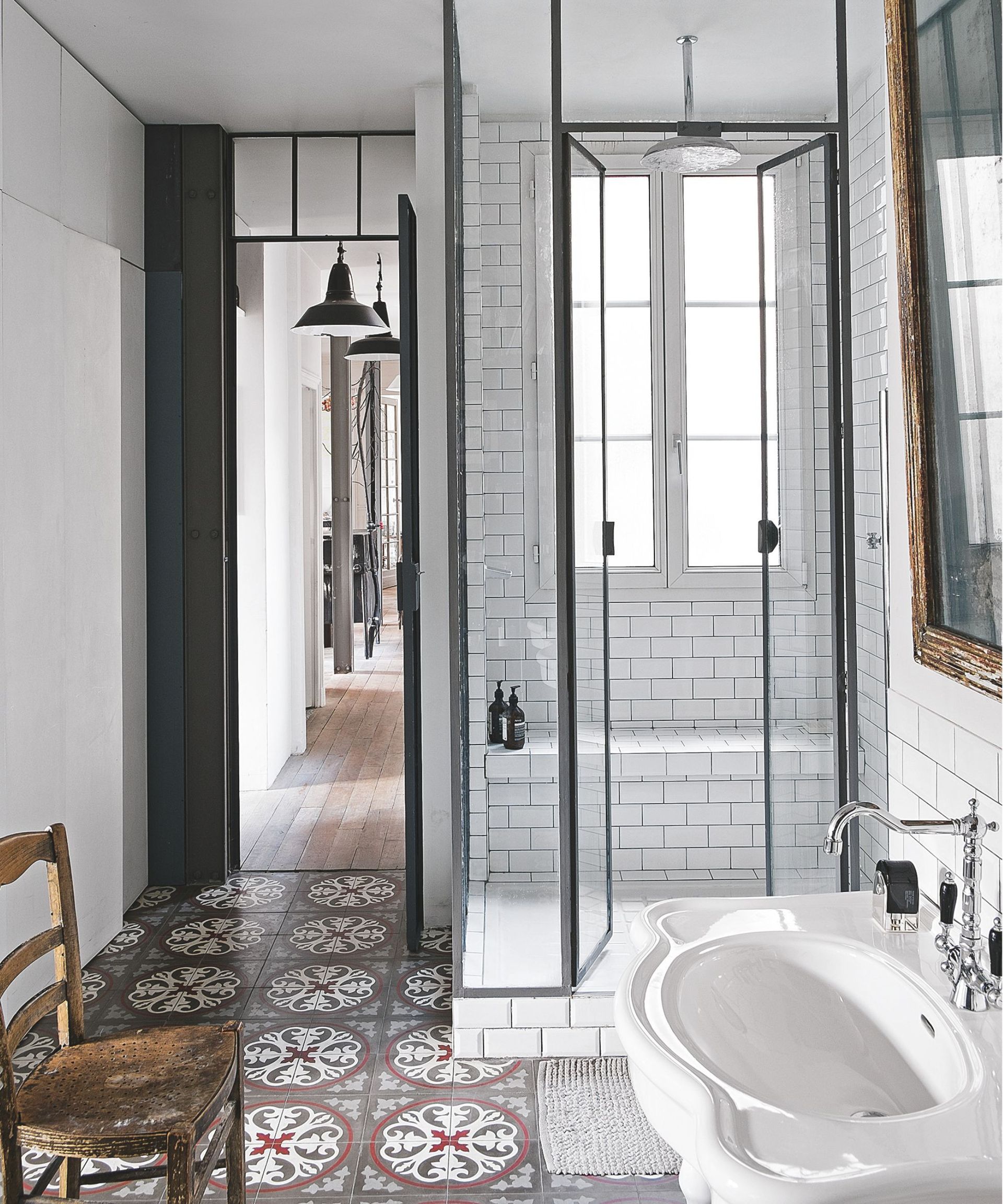 White and black shower with vintage tiling, a white sink with silver faucet and a brown wooden chair.