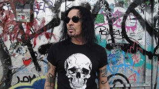 Jizzy Pearl standing against a graffiti'd wall.