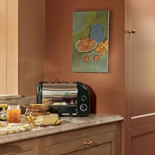 Italian inspired kitchen with black toaster and toast supplies on marble work top with gren and orange artwork on wall depicting peaches and blue jug