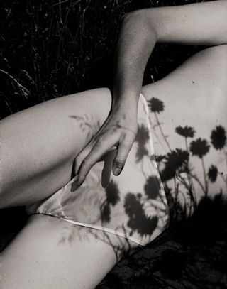 A faceless woman laying in the fields wearing white knickers.