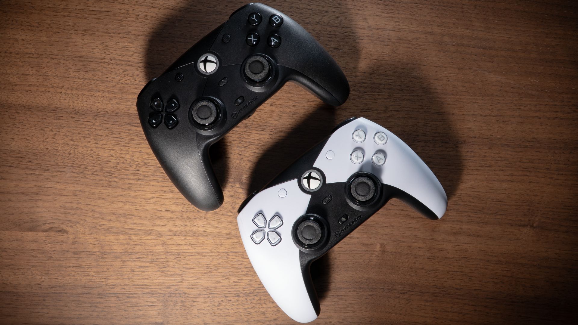 The White and Black Hyperkin Competitor controllers from above, lying on a wood desk