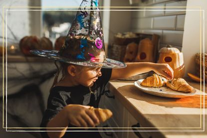 A young girl dressed up as a witch holding a croissant