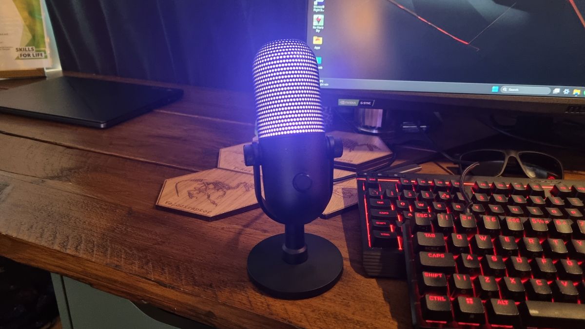 The Razer Seiren V3 Chroma desktop microphone, standing on a desk and lit up in pink